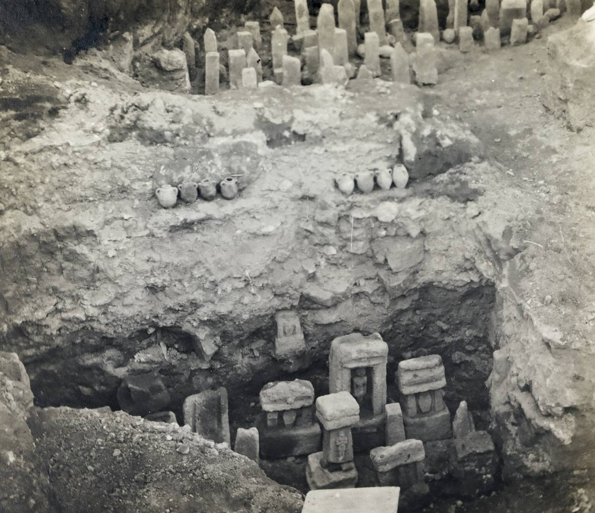 Photographie ancienne, en noir et blanc, représentant des objets archéologiques sur des monticules de terre.